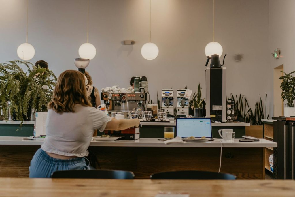 A woman works on a laptop at a coffee shop counter creating a productive workspace vibe.